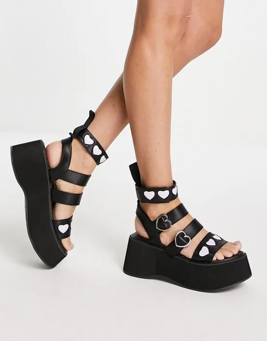 https://images.styletyx.com/images/koi-lovergirl-flatform-sandals-in-black-with-3d-hearts-koi-footwear-1739276_1.webp