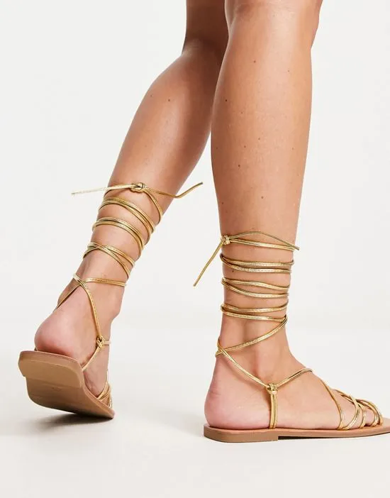 https://images.styletyx.com/images/strappy-tie-leg-flat-sandals-in-gold-london-rebel-wide-fit-13315870_2.webp