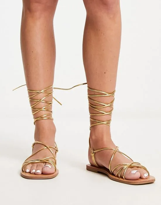 https://images.styletyx.com/images/strappy-tie-leg-flat-sandals-in-gold-metallic-london-rebel-13215597_1.webp