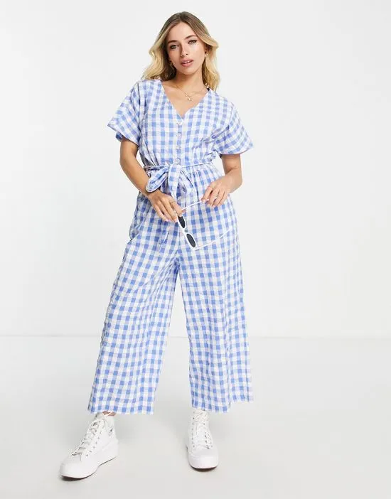 https://images.styletyx.com/images/tie-waist-seersucker-jumpsuit-in-blue-gingham-monki-2788748_1.webp